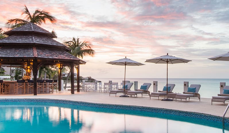 Veronica Bar Oceanfront resort swimming pool deck featuring a gazebo bar, lounge chairs under sun umbrellas, and panoramic sunset views over the ocean at Blue Waters Resort & Spa by Kenwood Travel