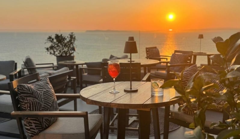Adults Only Lounge Bar Outdoor rooftop lounge bar with wooden tables, patio chairs, and cocktails served against a golden ocean sunset at Elix, Mar-Bella Collection by Kenwood Travel