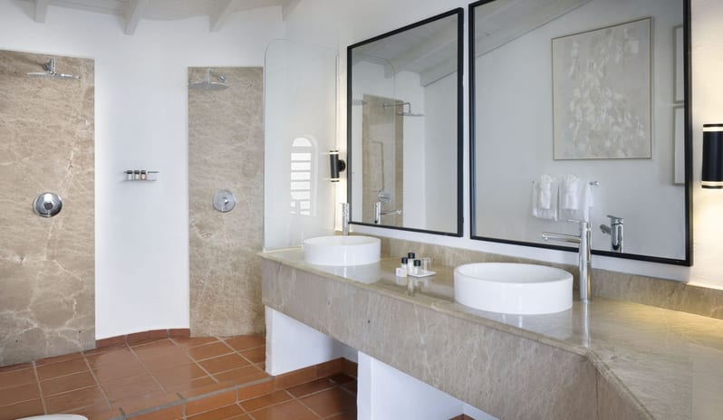 Dukes Manor Modern villa master bathroom suite with dual vessel sinks, stone countertops, double vanity mirrors, and luxury rainfall showers at Windjammers Landing by Kenwood travel