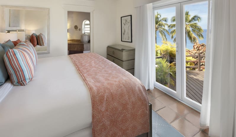 Dukes Manor Luxury beach resort master bedroom suite with king size bed, terracotta accents, ensuite bath access, and private terrace overlooking tropical greenery and the ocean at Windjammers Landing by Kenwood travel