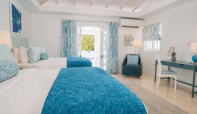 Presidential Manor Bright villa bedroom featuring two queen beds with textured blue throw blankets, patterned blue curtains, a dark blue armchair, and a teal vanity desk at Windjammers Landing by Kenwood travel