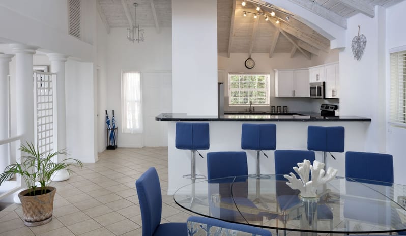 Prime minister Manor Luxury beach villa open dining room and modern kitchen counter with royal blue bar stools, glass table, and coral centerpiece at Windjammers Landing by Kenwood travel