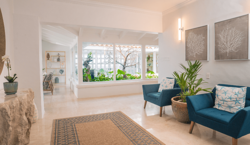 Presidential Manor Luxury resort hallway seating area with modern blue accent chairs, stone console table, tropical potted plant, and interior garden views at Windjammers Landing by Kenwood travel