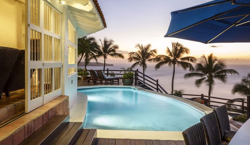 Governor Manor Spacious Luxury oceanfront villa infinity pool at dusk featuring a sun deck, palm silhouettes, and a blue patio umbrella at Windjammers Landing by Kenwood travel
