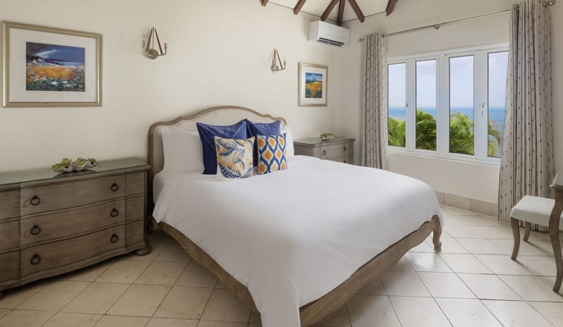 Royal Manor Luxury coastal villa master bedroom featuring a king bed, rustic wooden furniture, air conditioning, and scenic ocean and palm tree views at Windjammers Landing by Kenwood travel