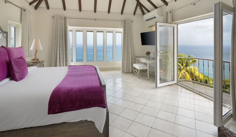 Royal Manor Spacious Sunlit hotel bedroom with purple bedding accents and wide windows and balcony doors facing the sea at Windjammers Landing by Kenwood travel