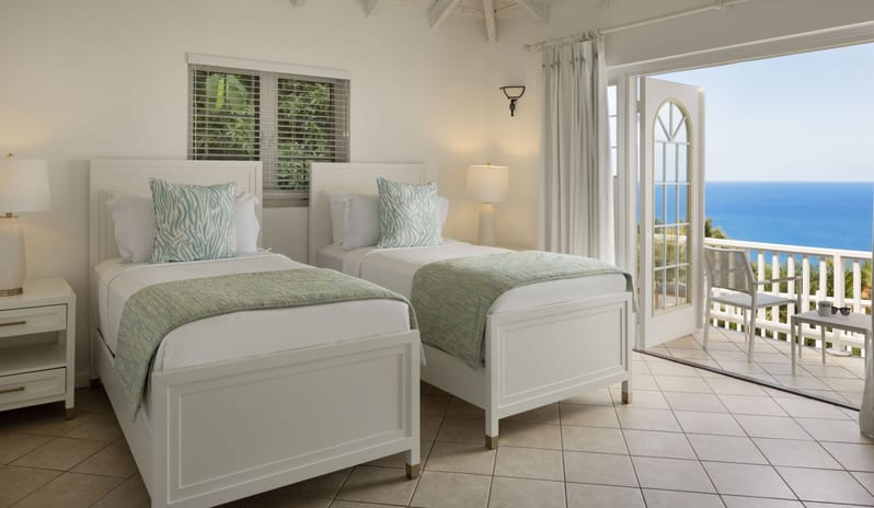 Prime minister Manor Bright coastal bedroom with two white twin beds, mint green bedding accents, and glass patio doors open to a oceanfront balcony at Windjammers Landing by Kenwood travel