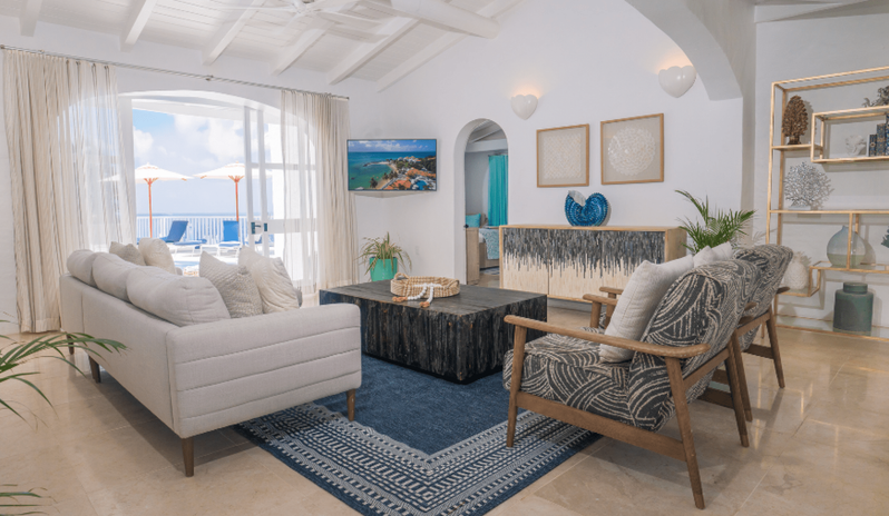 Presidential Manor Luxury beach resort living room suite with modern seating, gold display shelves, wall-mounted TV, and glass doors opening to a sun deck with pool umbrellas at Windjammers Landing by Kenwood travel