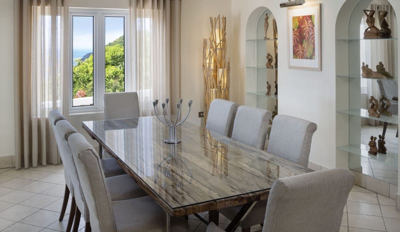 Royal Manor Luxury Luxury villa dining room set for eight guests, featuring modern decor, driftwood floor lamp, and scenic window views at Windjammers Landing by Kenwood travel