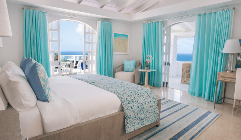 Presidential Manor Luxury beach resort master suite with oceanfront balcony access, vibrant turquoise curtains, plush king bedding, and a cozy seating nook at Windjammers Landing by Kenwood travel