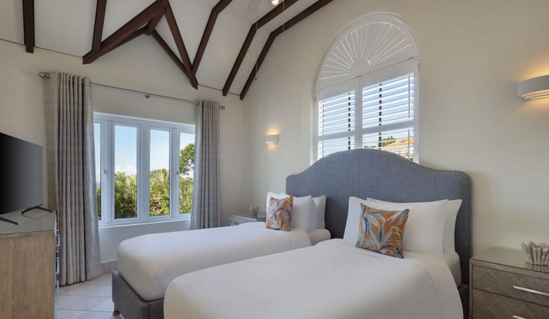 Royal Manor Spacious Luxury beach resort twin bedroom suite featuring plush grey-blue headboard, flat-screen TV, tropical accent pillows, and soft wall lighting at Windjammers Landing by Kenwood travel