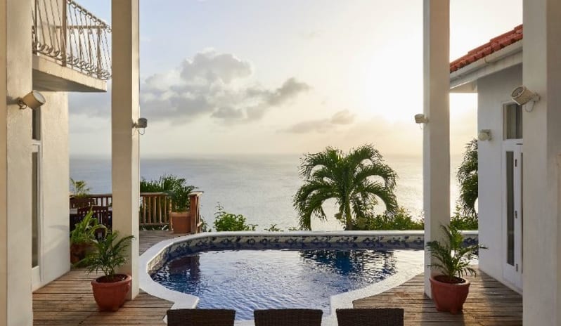 Dutchess Manor Private villa outdoor patio featuring a swimming pool, wooden deck, outdoor dining table, and direct ocean view at sunset at Windjammers Landing by Kenwood travel