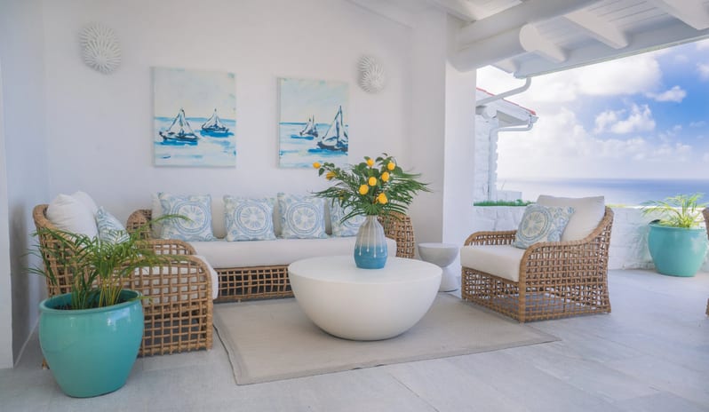 Presidential Manor Bright luxury covered patio featuring wicker seating with white cushions, coastal sailboat wall art, potted plants, a round coffee table, and an open view of the ocean at Windjammers Landing by Kenwood travel