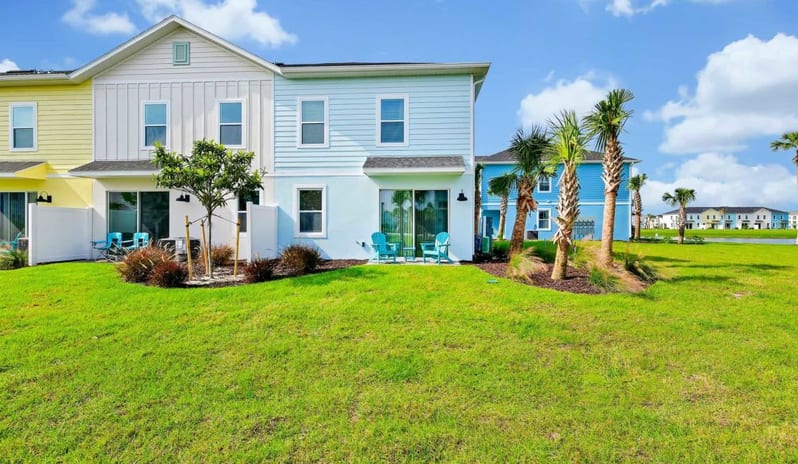 Four Bedroom Villa Backyard patio and lawn of a light blue coastal townhome surrounded by palm trees at Margaritaville Resort Orlando by Kenwood Travel