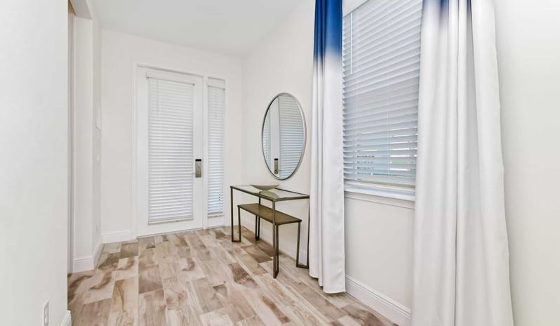 Four Bedroom Villa Bright entryway featuring a console table, oval mirror, and white front door with blinds at Margaritaville Resort Orlando by Kenwood Travel