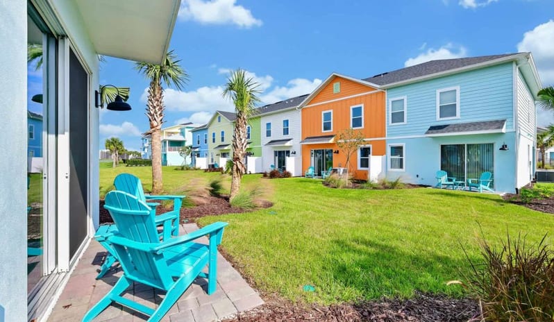 Four Bedroom Villa Bright blue patio chairs on a paved patio looking out at colorful coastal townhouses at Margaritaville Resort Orlando by Kenwood Travel