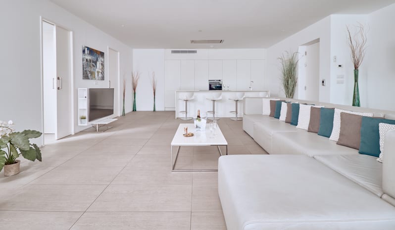 Divine Breeze Open-plan luxury penthouse living room showing a large sectional, television, coffee table with wine glasses, and a full modern kitchen setup at Domes Baobab by Kenwood Travel