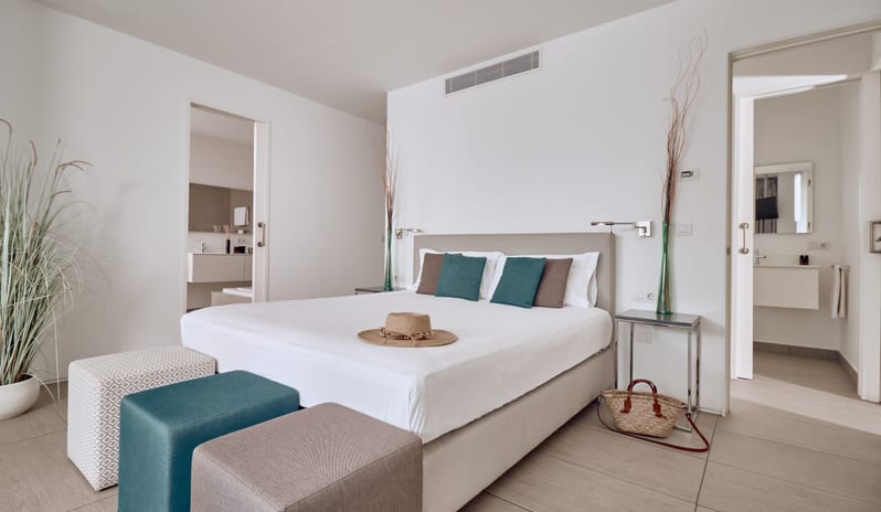 Divine Breeze Spacious luxury villa bedroom suite featuring a king bed, straw tote bag, woven hat, and en-suite bathroom access at Domes Baobab by Kenwood Travel