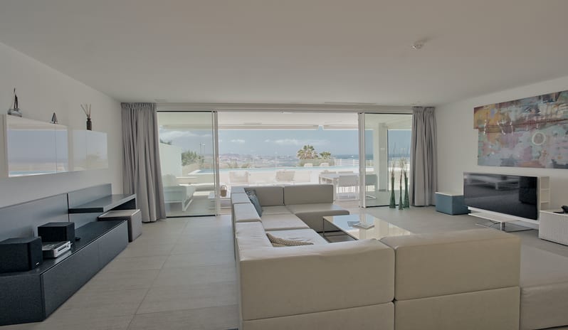 Divine Breeze Spacious villa lounge with a cream-colored sectional sofa, low coffee table, flat screen TV, and panoramic glass doors overlooking a sun terrace at Domes Baobab by Kenwood Travel