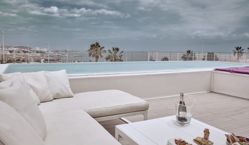 Divine Breeze Resort-style luxury villa rooftop deck with private infinity pool, cushioned outdoor sofa, iced champagne, and tapas set on a low table at Domes Baobab by Kenwood Travel