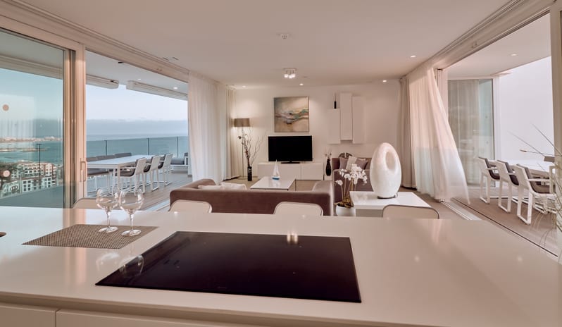 Serenity Allegra Bright, luxury open-concept apartment interior with a sleek kitchen island, cozy living area with TV, and balconies featuring outdoor dining sets at Domes Baobab by Kenwood Travel