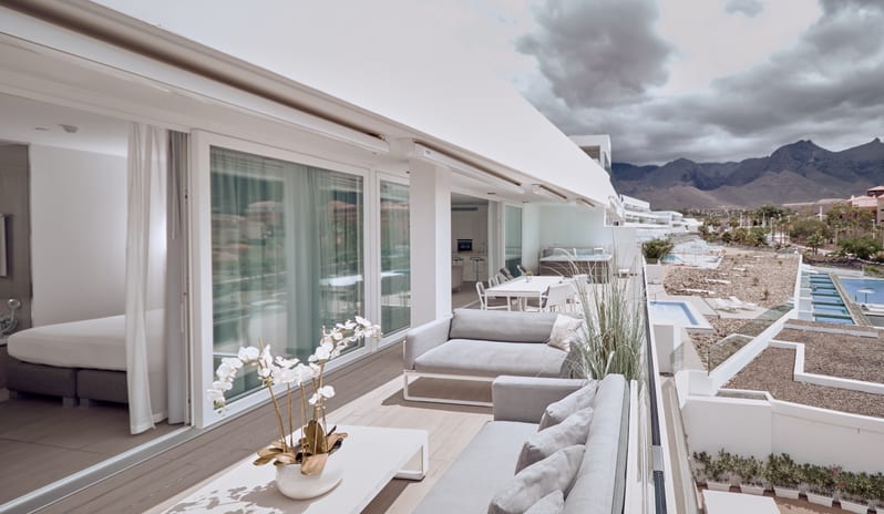 Serenity Allegra Bright, Luxury white penthouse balcony equipped with patio furniture, offering a scenic view of surrounding resorts and mountains under a cloudy sky at Domes Baobab by Kenwood Travel