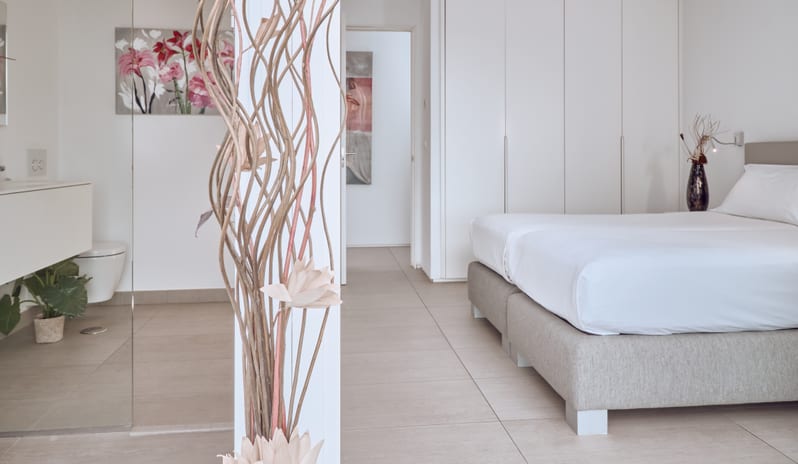 Serenity Allegra Clean and spacious luxury bedroom suite with neutral floor tiles, white closets, and a glass-partitioned modern bathroom at Domes Baobab by Kenwood Travel