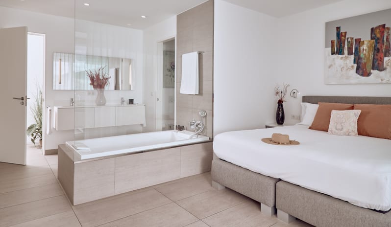 Serenity Allegra Modern open-concept master suite featuring a double bed with terracotta pillows and a large glass-partitioned bathtub connected to the bedroom at Domes Baobab by Kenwood Travel