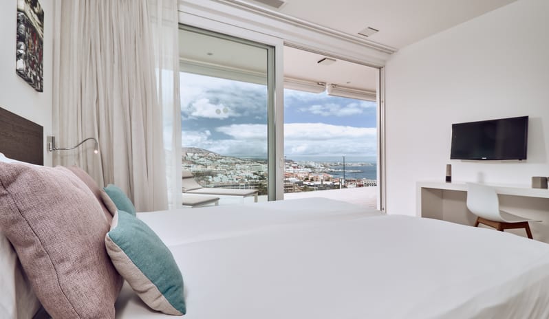 Serenity Essence Bright resort suite bedroom featuring a king bed, work station, and large sliding doors leading to a sun deck overlooking the coastal city and sea at Domes Baobab by Kenwood Travel