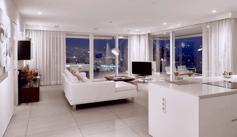 Serenity Elegance Contemporary open-plan apartment interior with sleek white furnishings, recessed lighting, and sheer white curtains framing a night cityscape at Domes Baobab by Kenwood Travel