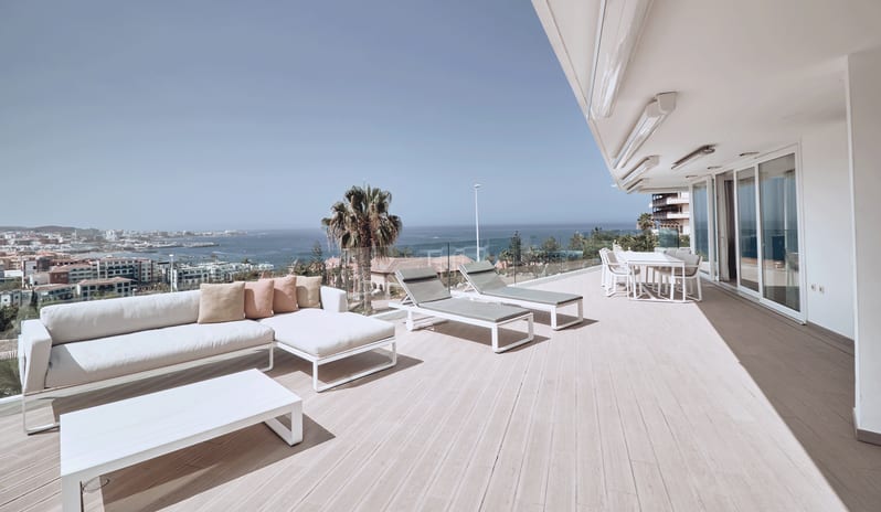 Serenity Elegance Modern villa patio with comfortable outdoor lounge furniture, sunbeds, glass railings, and sweeping views of the sea under a clear sky at Domes Baobab by Kenwood Travel