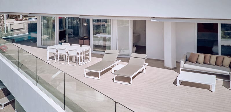 Serenity Elegance Modern penthouse balcony with outdoor lounge chairs, a shaded dining area, and an L-shaped sofa overlooking a pool below at Domes Baobab by Kenwood Travel
