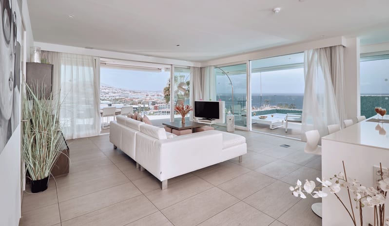 Serenity Elegance Spacious villa interior with modern white furniture, sliding glass doors opening to a private pool terrace, and sweeping coastal views at Domes Baobab by Kenwood Travel
