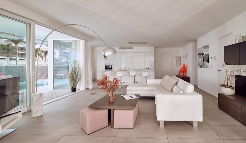 Serenity Elegance Luxury villa interior with modern white furnishings, kitchen island with bar stools, and direct patio access to a private outdoor pool at Domes Baobab by Kenwood Travel