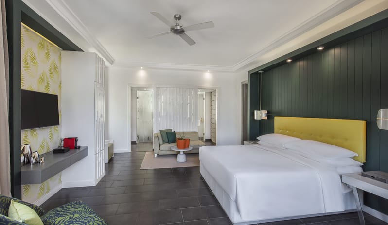 Family Suite king bed with yellow leather headboard, spacious living lounge, TV entertainment console, and ceiling fan at Long Beach Mauritius by Kenwood Travel
