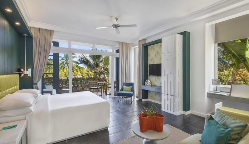 Family Suite bedroom with king bed, sofa lounge, wall-mounted TV console, and wide glass doors opening to a private garden terrace at Long Beach Mauritius by Kenwood Travel