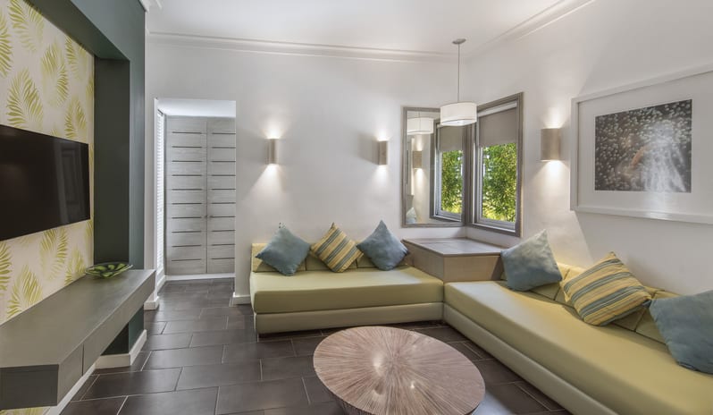 Family Suite living room featuring an L-shaped corner daybed sofa, wooden coffee table, wall sconce lighting, and wall-mounted TV console at Long Beach Mauritius by Kenwood Travel