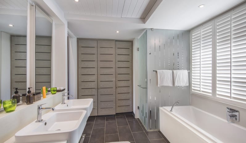 Junior Suitebathroom featuring double basin sinks, deep soaking bathtub, frosted glass shower enclosure, and white shutter window at Long Beach Mauritius by Kenwood Travel