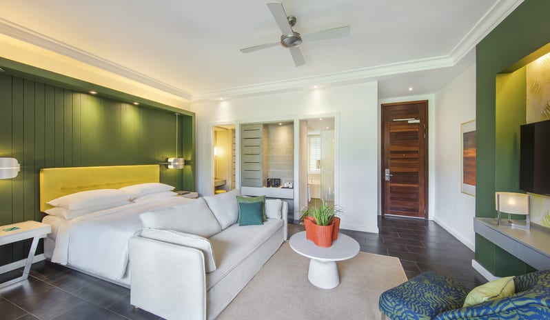 Junior Suite Premium king bed with yellow headboard, white sofa, coffee table, and green accent walls at Long Beach Mauritius by Kenwood Travel