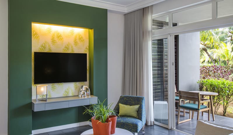 Junior Suite Premium wall-mounted TV, comfortable sofa, coffee table, and glass doors opening to a garden terrace at Long Beach Mauritius by Kenwood Travel