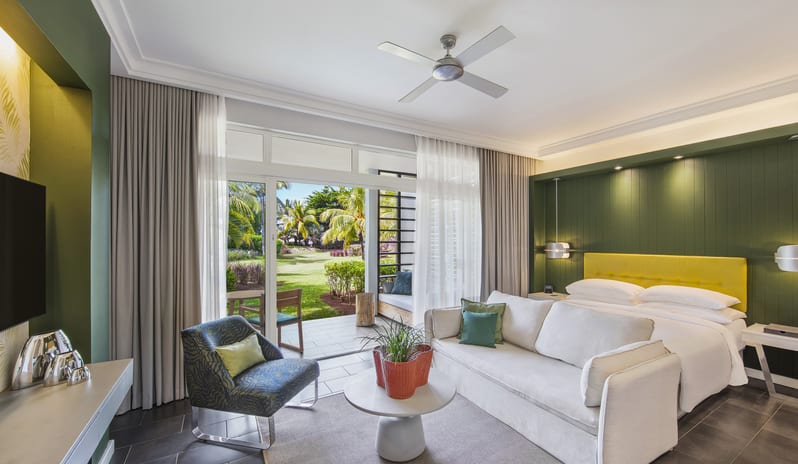 Junior Suite living area featuring a king bed with yellow headboard, sofa, accent armchair, and open sliding doors leading to a private garden patio at Long Beach Mauritius by Kenwood Travel