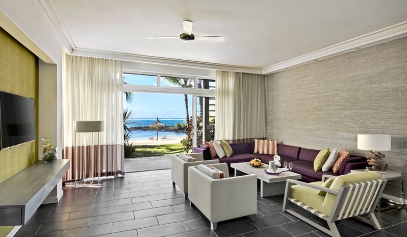 Long Beach Executive Suiteliving room with purple sectional sofa, lounge armchairs, TV console, and wide glass doors opening to a beachfront ocean view at Long Beach Mauritius by Kenwood Travel