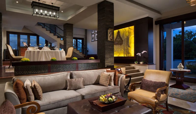 Royal Samabe Residence dining tfeaturing a split-level design with a cozy sofa lounge, leather armchairs, and an elevated formal dining area with staircase at Samabe Bali Suites and Villas by Kenwood Travel