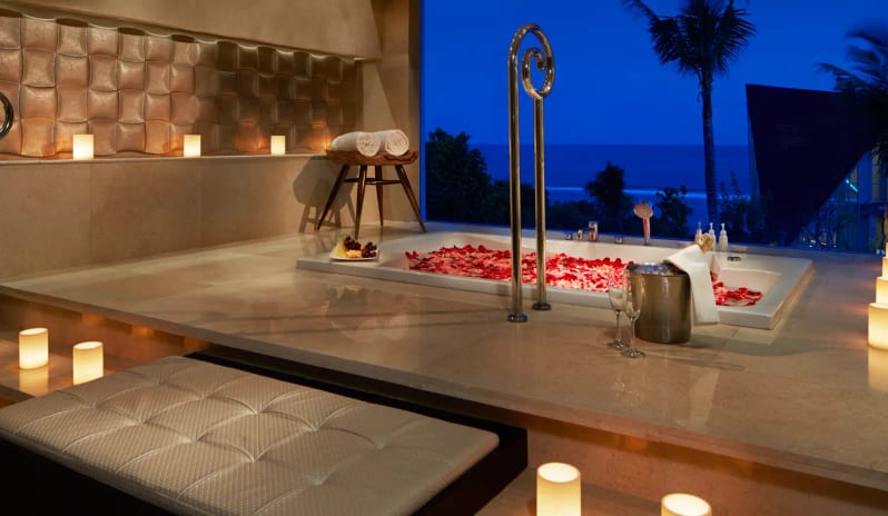 Royal Samabe Residence dining unken marble bathtub filled with rose petals, surrounded by glowing candles and champagne overlooking the ocean at night at Samabe Bali Suites and Villas by Kenwood Travel