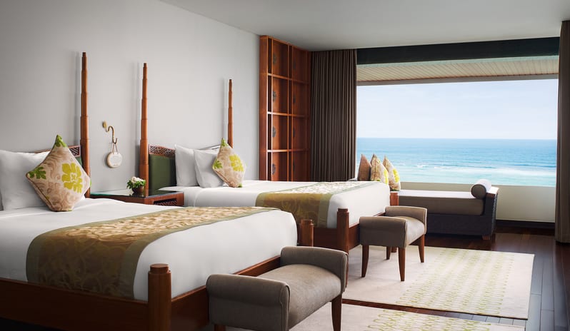 Ocean Front Family Suite two queen beds, bed benches, daybed, and large picture window overlooking the blue ocean at Samabe Suites & Villas by Kenwood Travel