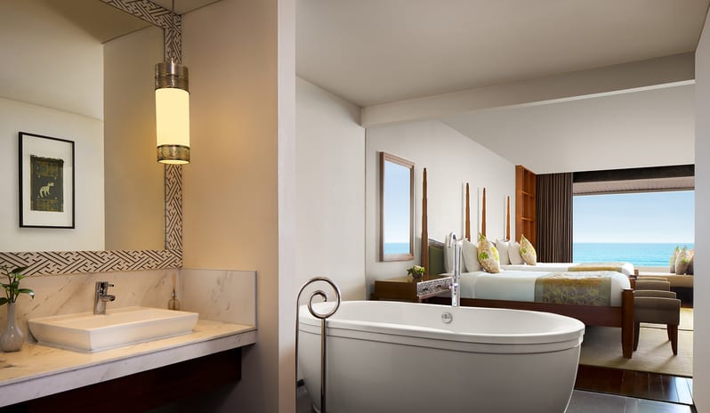 Ocean Front Family Suite open ensuite bathroom featuring a freestanding oval bathtub, marble vanity sink, and view into the bedroom overlooking the ocean at Samabe Suites & Villas by Kenwood Travel