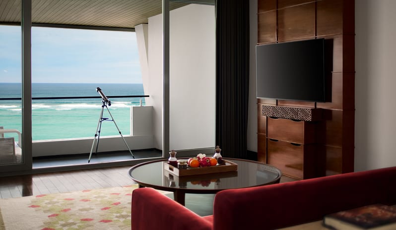 Ocean Front Family Suite featuring a flat-screen TV console, round coffee table with fresh fruit platter, and private balcony with telescope overlooking the turquoise ocean at Samabe Suites & Villas by Kenwood Travel