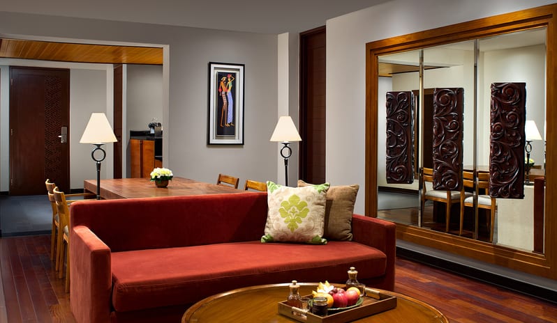 Ocean Front Family Suite terracotta red sofa, round wooden coffee table with fresh fruit platter, dining table, and large framed wall mirror at Samabe Suites & Villas by Kenwood Travel