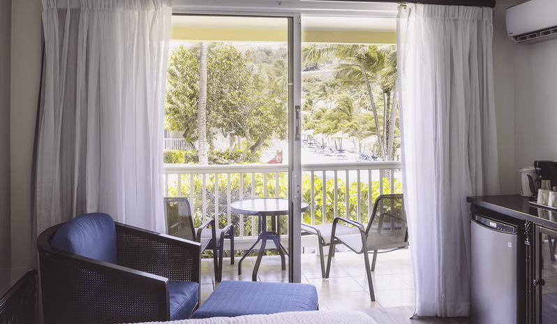 Club Room Garden View sliding glass doors opening to a private balcony with outdoor seating and lush resort grounds view at St James’s Club & Villas by Kenwood Travel