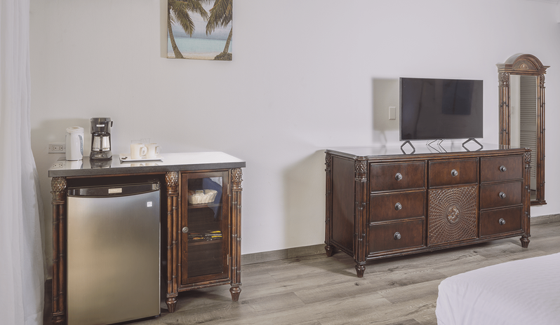 Club Room Garden View entertainment and amenity area featuring a flat-screen TV on a carved wood dresser, a mini fridge station with coffee maker, and full-length mirror at St James’s Club & Villas by Kenwood Travel